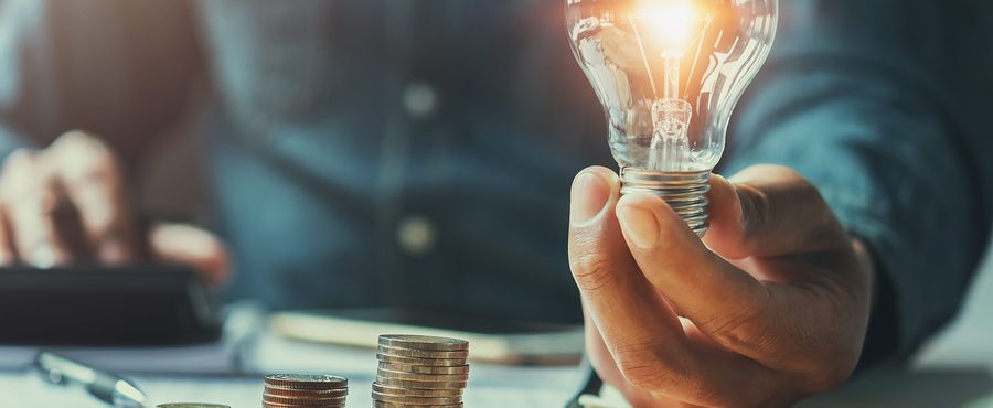 energy product financing; man holding lit lightbulb while calculating finances